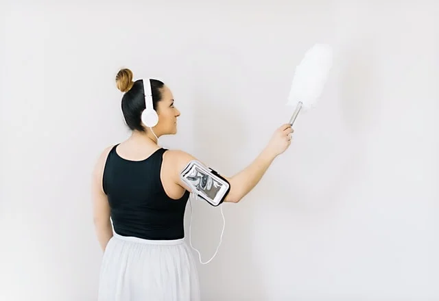 Woman wearing a headset dusting a wall which is one of the places you're probably forgetting to clean